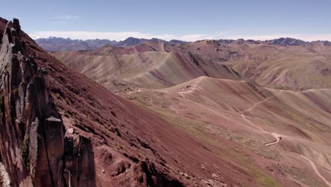 towering rock cliffs rise from the rugged terrain, highlighting a striking contrast between earthy tones and the clear blue sky. dry mountain valleys stretch out beyond the peaks.