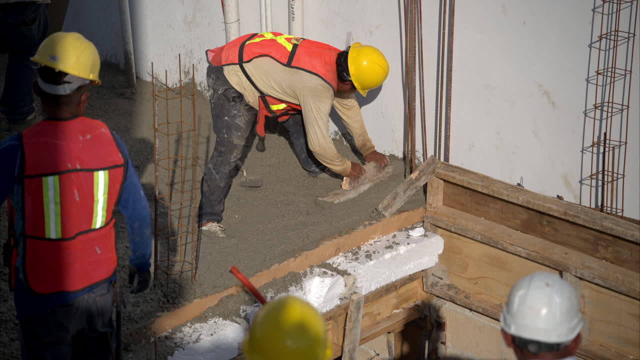 movimiento lento de un trabajador de la construcción latino mexicano aplanando el hormigón fresco usando una paleta de madera bajo el sol en una tarde calurosa con un casco