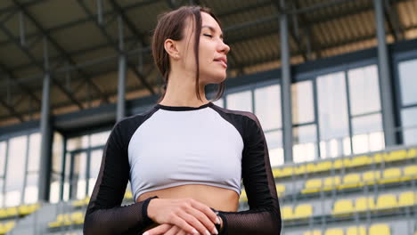 hermosa chica en forma sonriente descansando y revisando el reloj inteligente después de hacer ejercicio en el estadio