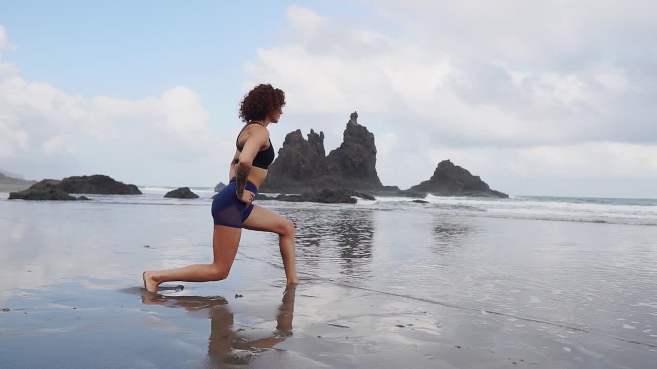 In slow motion, a young, slender woman performs stretching and yoga near the ocean's edge, her eyes fixed on the distant scenery