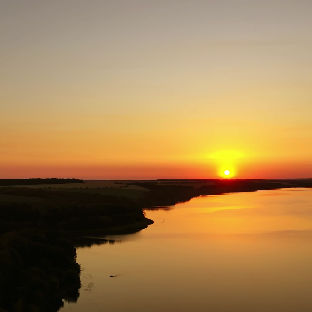Orange sunset. Beautiful view of river under colorful sky of the setting sun. Amazing sunset on water surface. Aerial view.