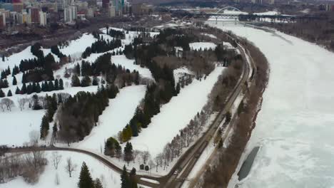 Vista-Aérea-De-Pájaro-Volar-Sobre-El-Parque-Victoria-Por-El-Río-Nevado-Helado-Del-Norte-De-Saskatchewan-Junto-Al-Valle-Del-Río-Ed-Nw-En-Una-Tarde-Sombría-De-Invierno-Rodeada-De-Parques-Tranquilos-Campos-De-Golf-6-7