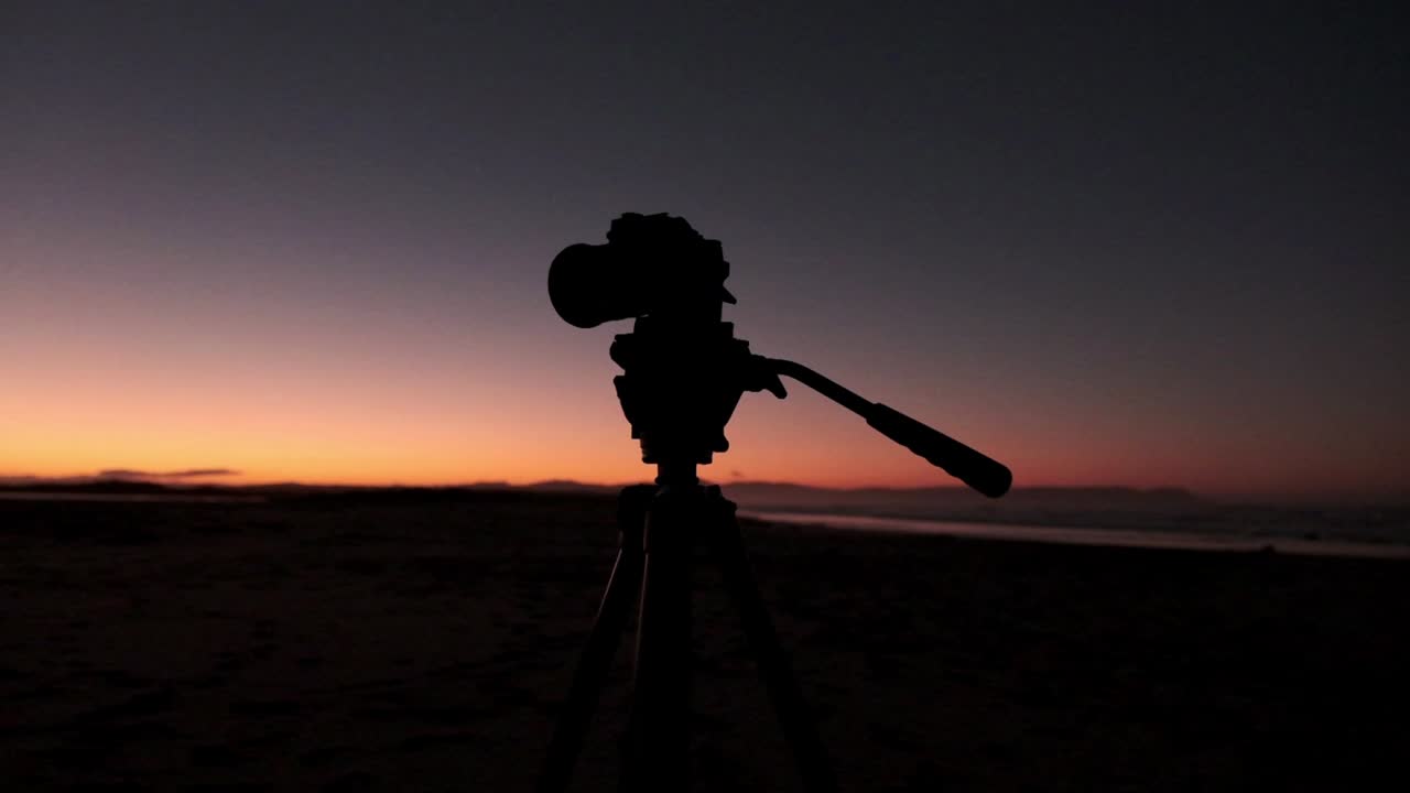 silhueta de uma câmera digital em um tripé ao amanhecer na praia