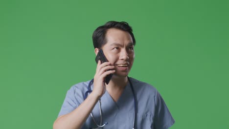 병원에서 녹색 화면 배경에서 걸어가는 동안 스마트폰으로 말하는 스테토스코프를 가진 아시아 남성 의사의 클로즈업