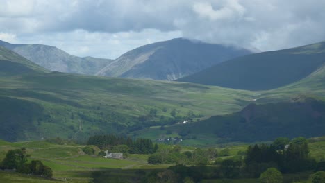 Dicke-Wolken-Ziehen-über-Berggipfel,-Während-Schatten-über-Eine-Grüne-Landschaft-Mit-Isolierten,-In-Hügel-Eingebetteten-Behausungen-Rasen