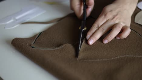 Close-view-of-female-hands-cutting-a-brown-fabric-with-scissors-on-table-in-atelier