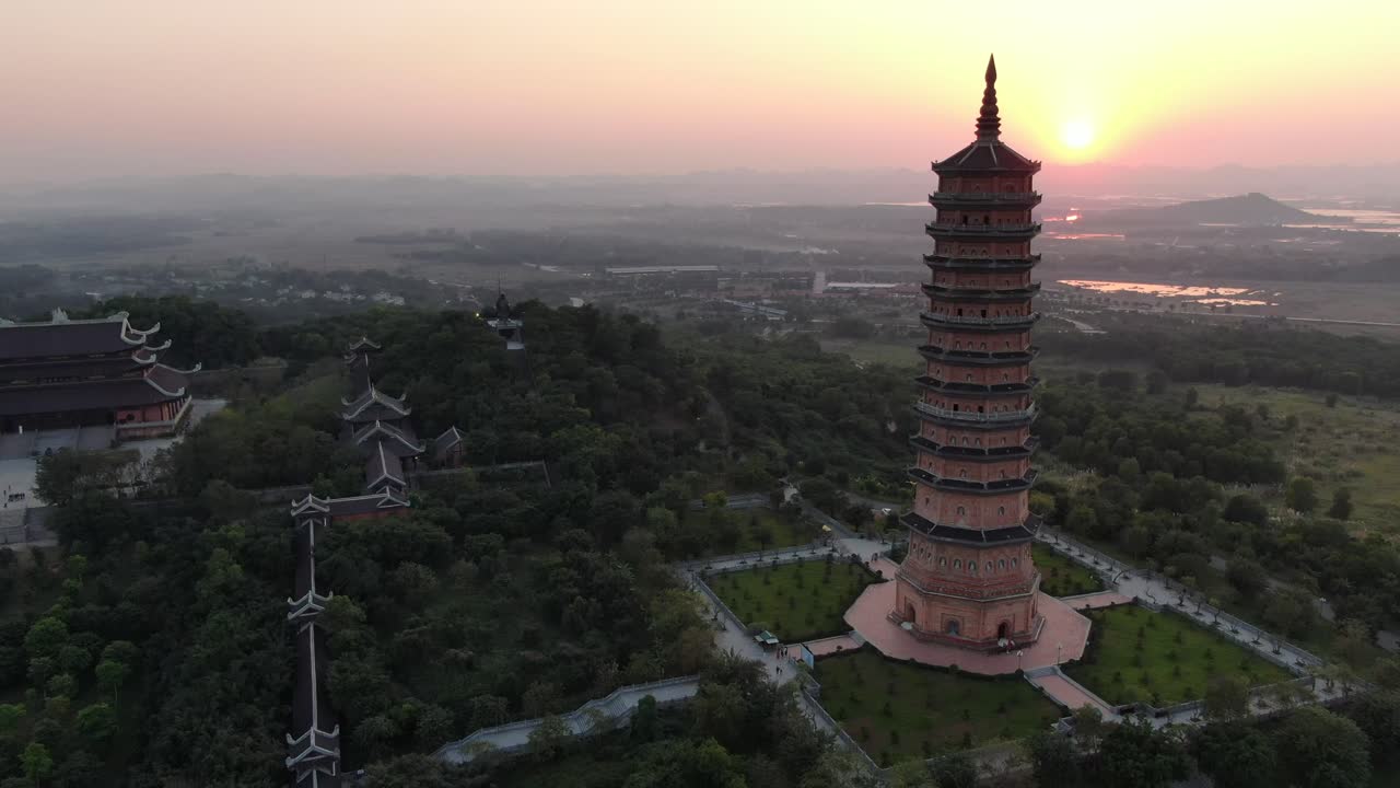 vista aérea de drones en vietnam volando sobre un área de templo budista llena de árboles verdes y una pagoda frente al sol en ninh binh al atardecer