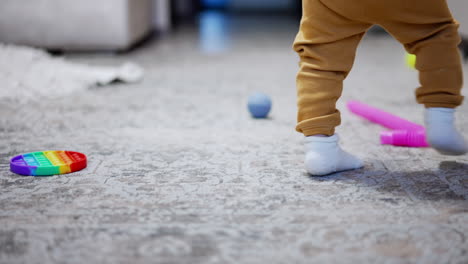 little feet of a baby in white socks. active baby boy runs by the carpet with scattered toys.
