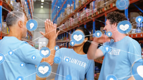 Animation-of-network-of-connections-with-icons-over-diverse-volunteers-working-in-warehouse