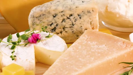 a curated display of various cheeses garnished with fresh herbs and flowers on a wooden board.