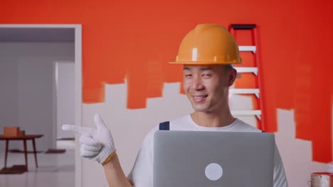 un contratista sonriente con una computadora portátil en una habitación recién pintada