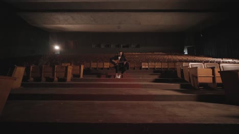 a handsome guy plays an acoustic guitar in an abandoned cinema. the musician sings a song and accompanies on the guitar