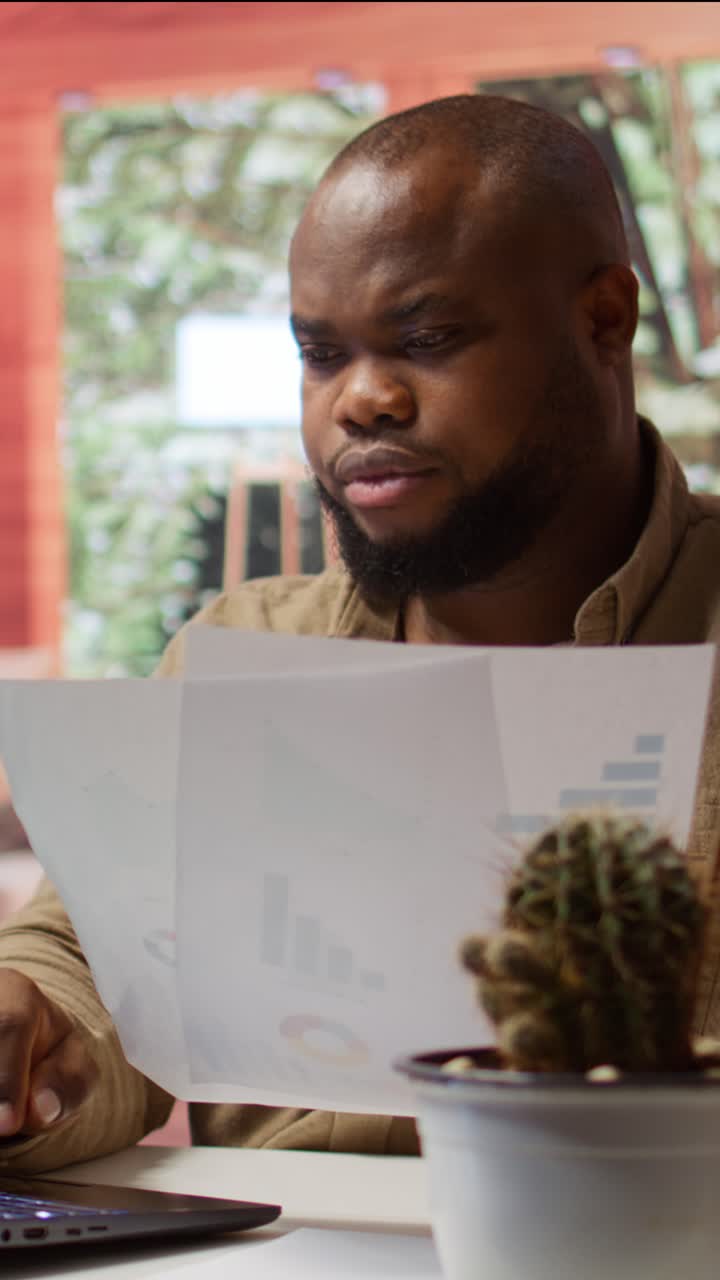 African American Man Analyzing Documents and Typing on Laptop