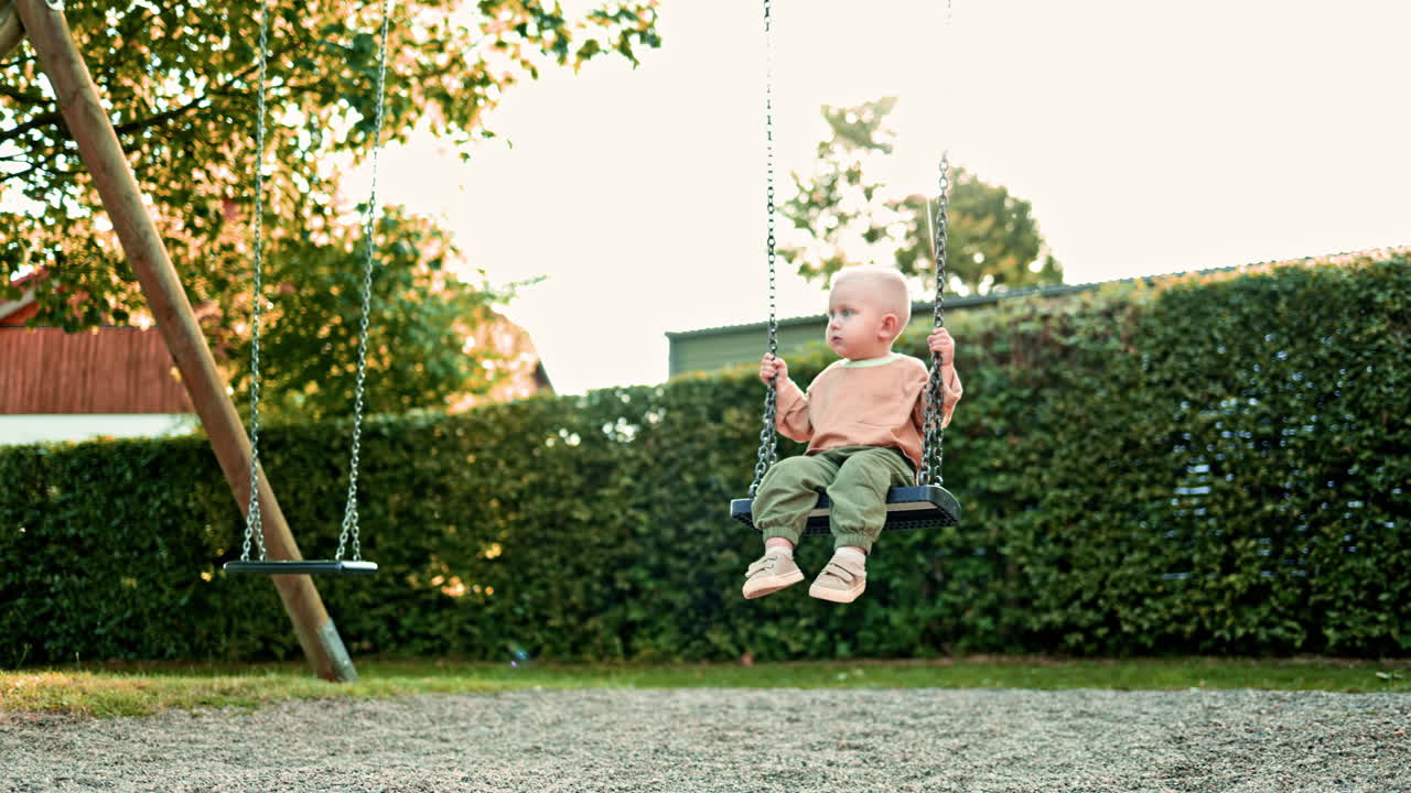 Happy boy swings on a swing on a playground in the park. The child has fun on a walk. Swing for children in a city park. Toddler boy rides on a swing in the summer. Children's entertainment