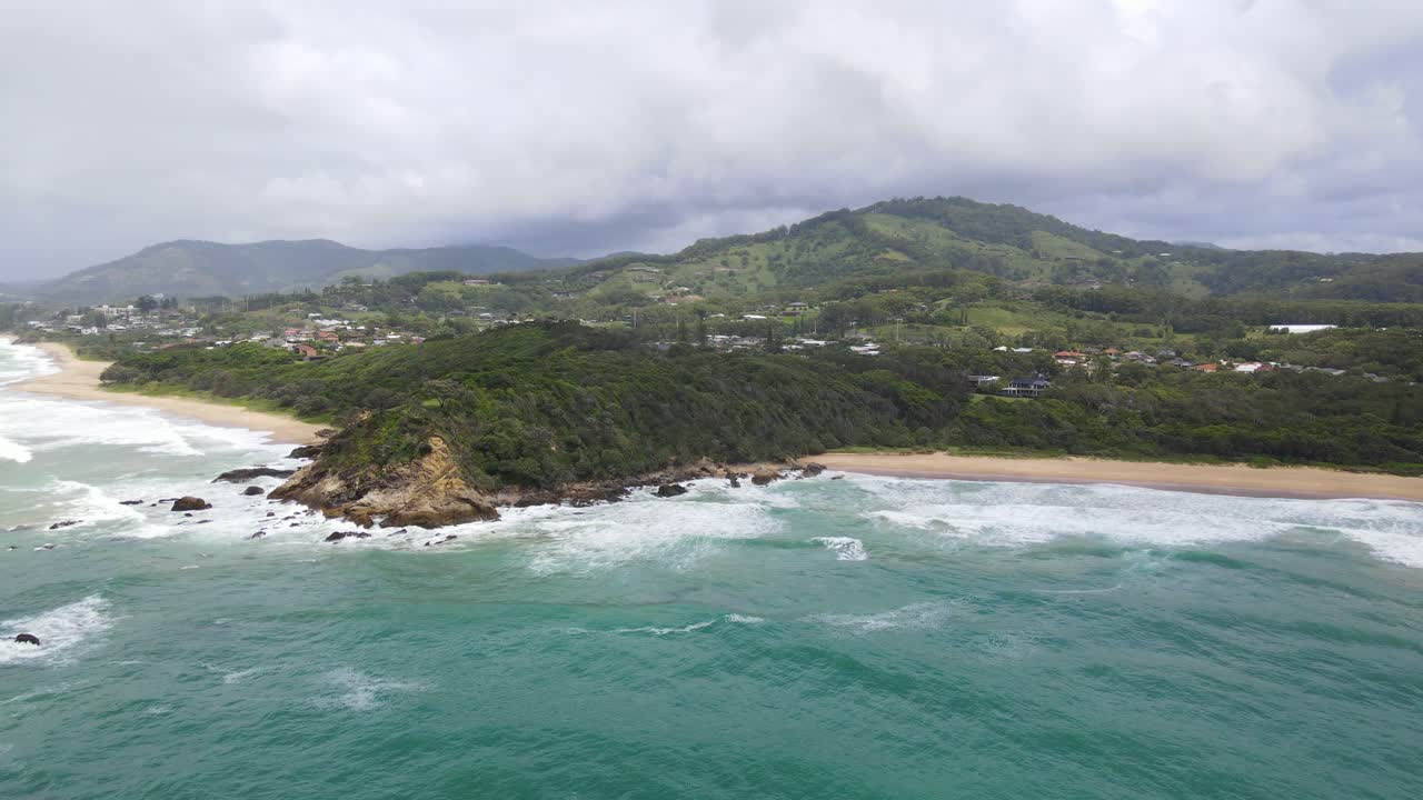 vuelo cinematográfico sobre el océano ondulado con un acantilado áspero y una ciudad costera en el fondo