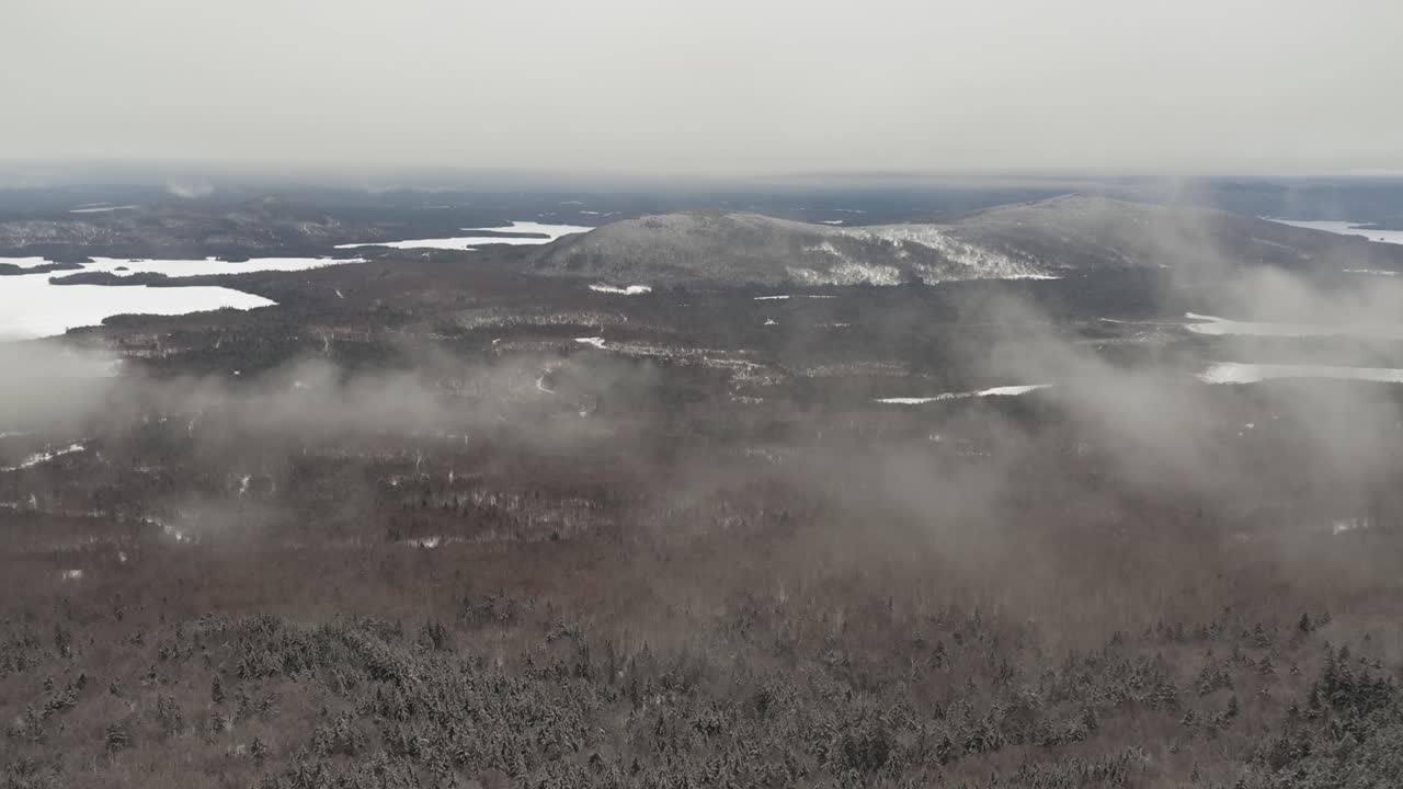 nubes bajas sobre un interminable bosque invernal con lagos y colinas aéreas
