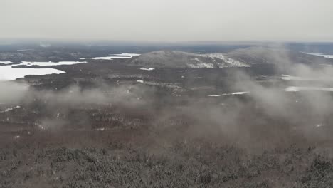 low hanging clouds over an endless winter forest with lakes and hills aerial