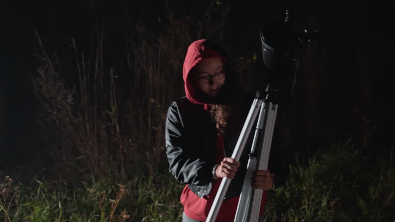 Night field stargazer prepares telescope, hooded hobbyist aligns tripod and peers into eyepiece near urban edge, distant city lights, quiet meadow, contemplative mood, patient search for star