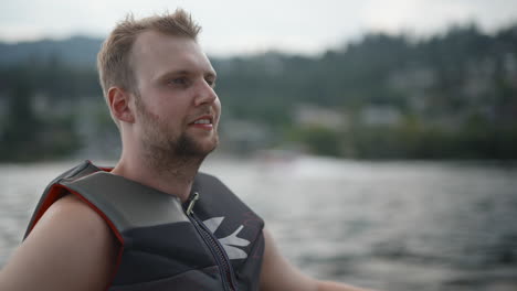 Close-up-man-in-life-vest-doing-water-sports-watches-boat-on-mountain-lake