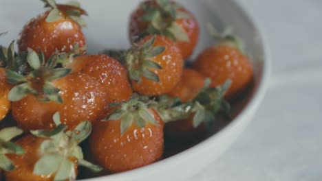 detalle de un tazón blanco de deliciosas fresas rojas, una mano llega y toma una