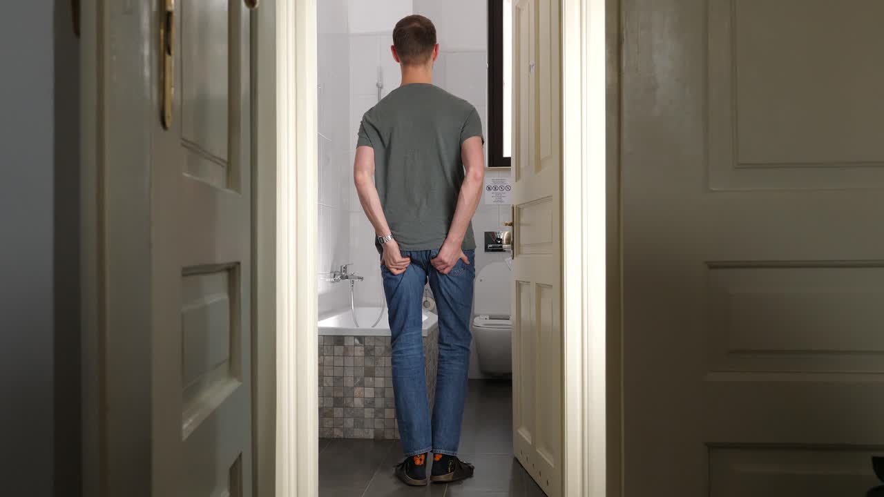 Young tall man go inside bathroom and feels sudden severe pain in anus area, holds buttocks and tear jeans