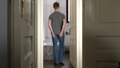 young tall man go inside bathroom and feels sudden severe pain in anus area, holds buttocks and tear jeans