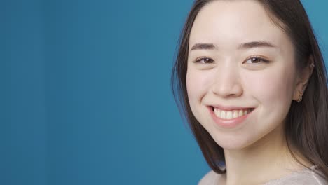 Asian-woman-looking-at-camera-and-laughing.-Blue-background.