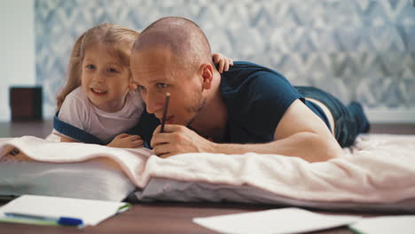 little girl whispers to dad ear lying on floor with blanket