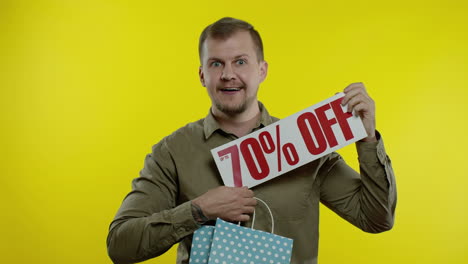 joyful man showing up to 70 percent off inscription from shopping bag, smiling, rejoicing discount