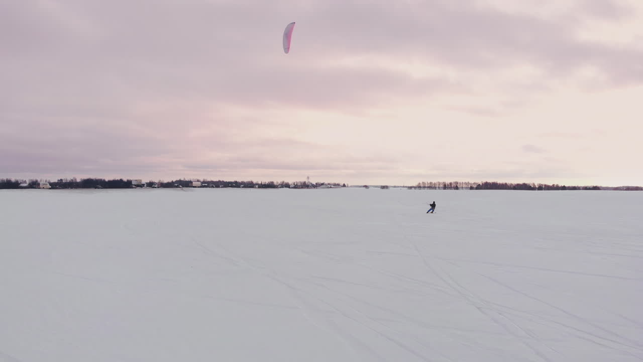 cámara lenta: un atleta masculino practica kitesurf en esquís. rueda sobre el hielo de un gran lago. rodando, realiza diversos saltos, golpes y otros ejercicios. día ventoso y soleado de invierno