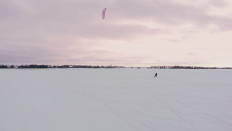 SLOW-MOTION:-A-male-athlete-is-engaged-in-kiting-on-skis.-He-rolls-on-the-ice-of-a-large-lake.-Rolling,-he-performs-various-jumps,-coups-and-other-exercises.-Windy-sunny-winter-day