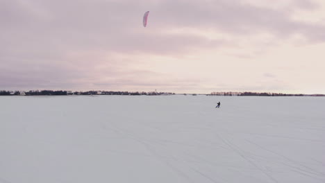 slow motion: a male athlete is engaged in kiting on skis. he rolls on the ice of a large lake. rolling, he performs various jumps, coups and other exercises. windy sunny winter day