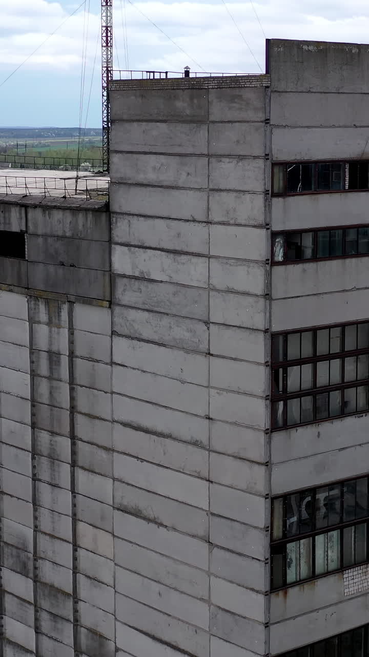 Tall old factory building on green nature background. Abandoned industry. Empty ruined industrial edifices in the countryside. Aerial view. Vertical video