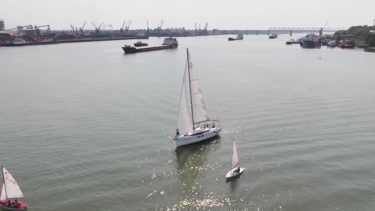 yate de vela en un río con barcos de carga
