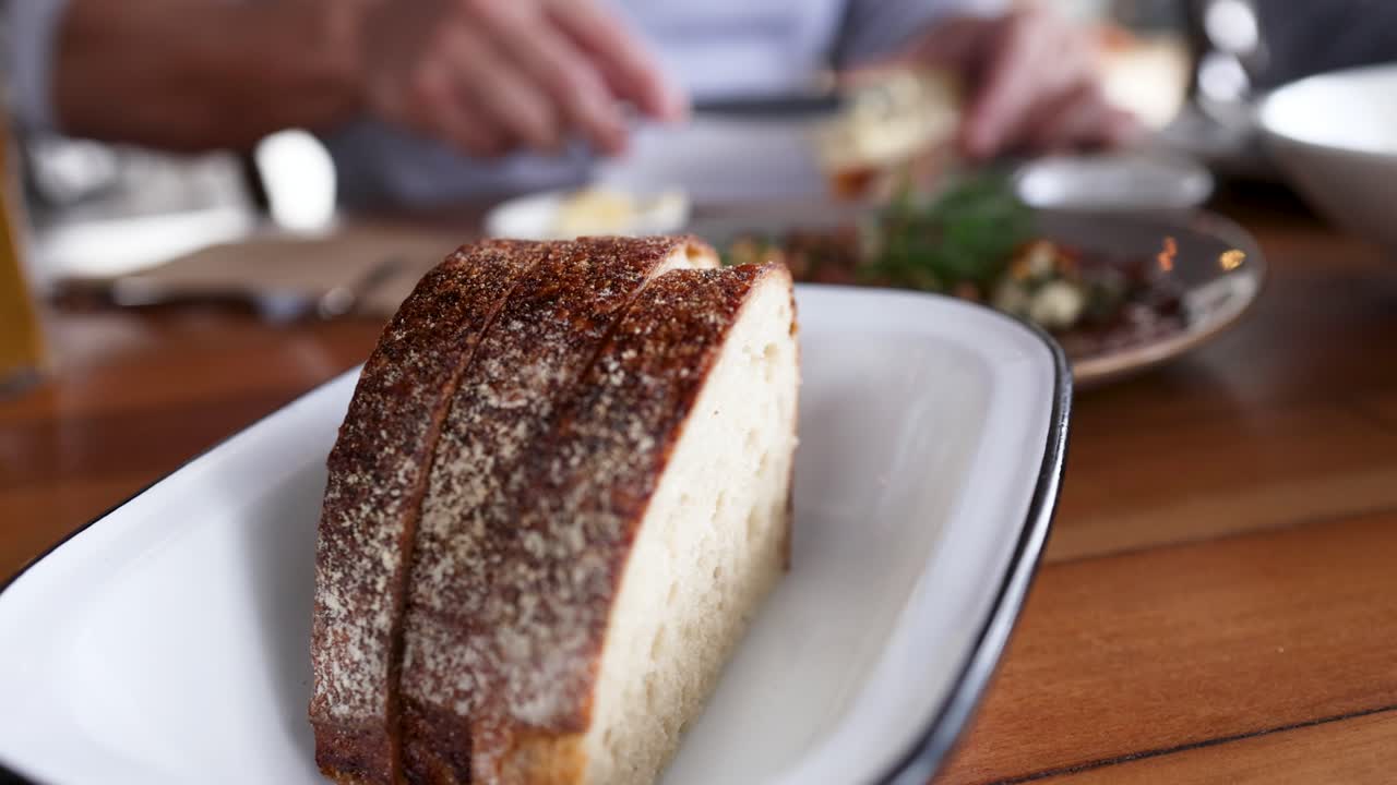 Hands prepare fresh bread with toppings on a wooden table, creating a warm and inviting atmosphere