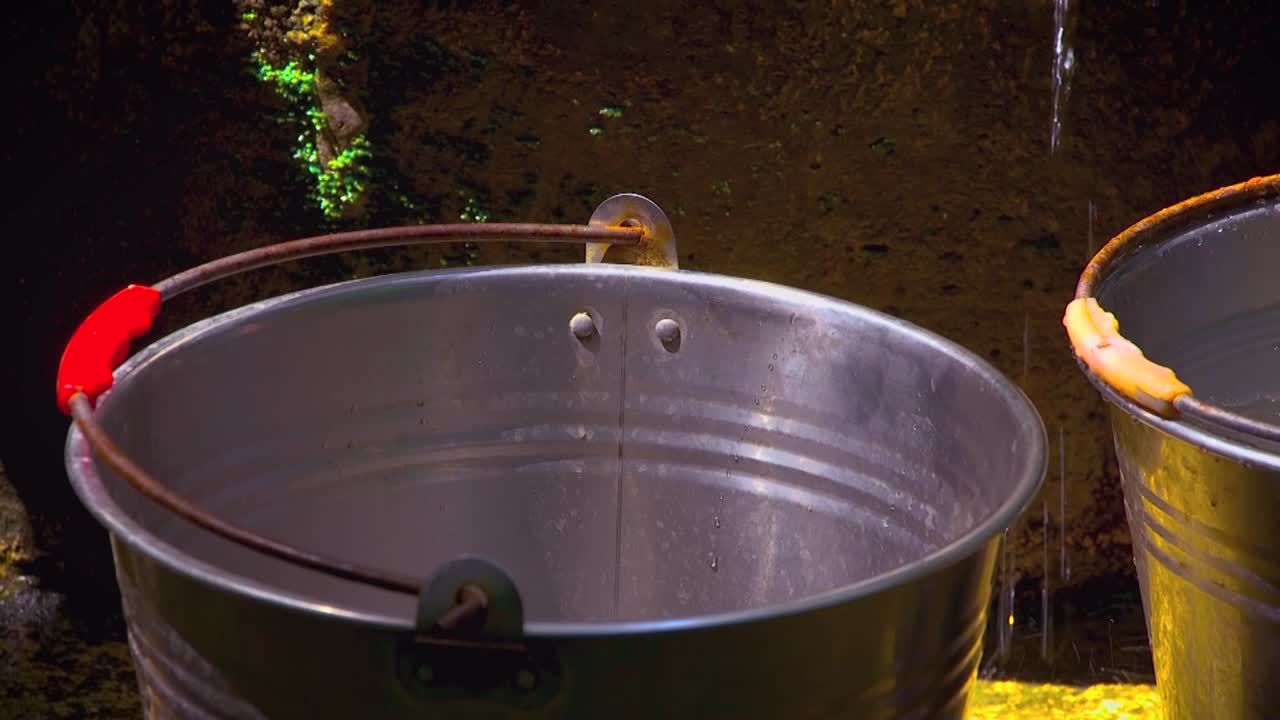 Water from a water well poured into metal buckets.