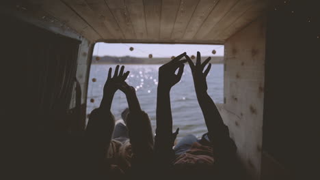 two girls are lying in the back of a caravan by a lake and move their hands sinuously