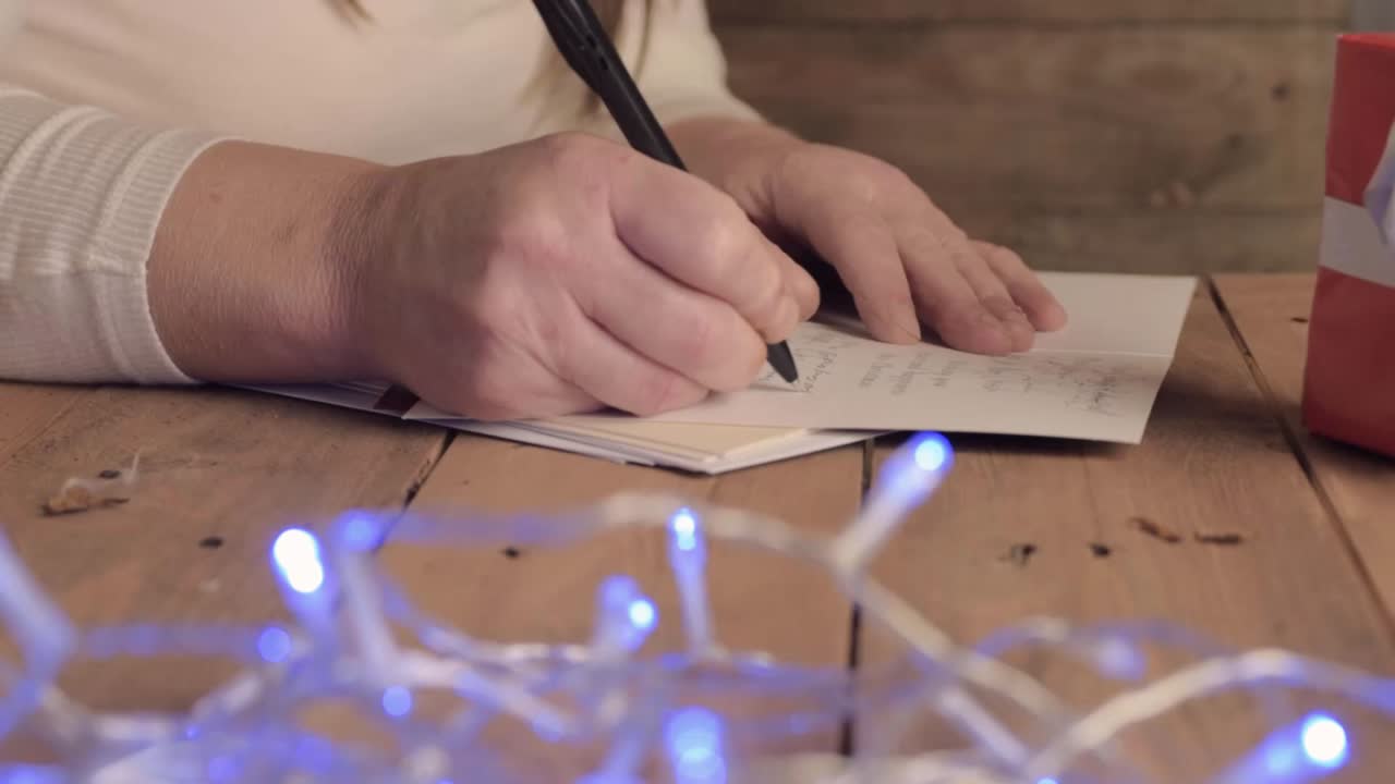 Woman writing out Christmas greeting cards with Christmas lights