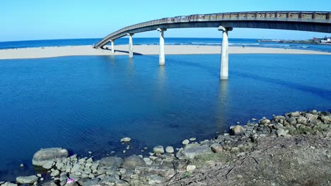 vuelo aéreo bajo el puente de agua y sobre la playa de arena de fulong en taiwán durante el cielo azul