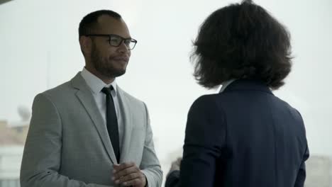 Smiling-business-partners-talking-in-hallway-near-window