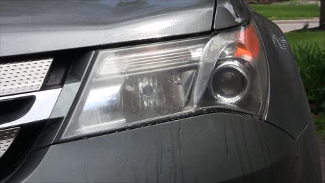 a person spraying water and wiping with a blue towel a headlight on an suv