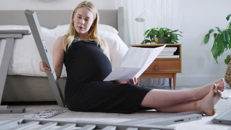 pregnant mother to be looking at instructions for self assembly baby cot in bedroom