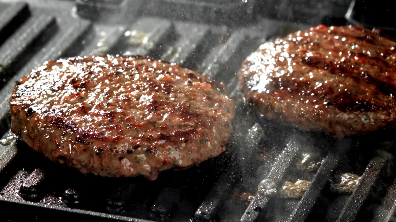 Two Hamburger Patties Sizzling on a Hot Grill Pan