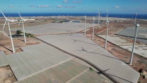 An-Einem-Sonnigen-Tag-überqueren-Wir-Ein-Feld-Aus-Windkraftanlagen-Und-Gewächshäusern-In-Einer-Wüstenlandschaft-Auf-Der-Insel-Gran-Canaria