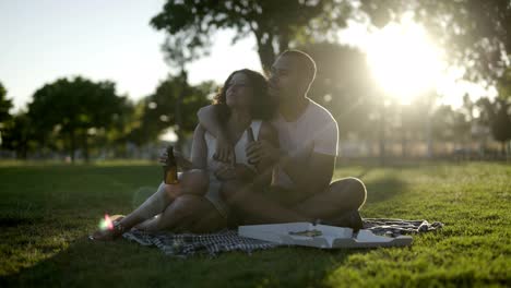 couple with beer and pizza in park