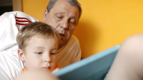 Grandfather-watching-grandson-playing-on-pad