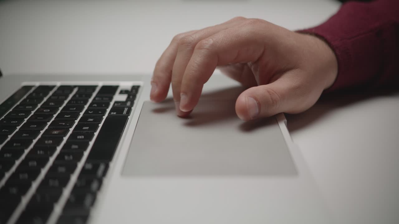 An extreme close-up shot of a man's fingers scrolling, tapping, and navigating on a laptop's trackpad. A concept of Browse, online work, and digital user interface interaction