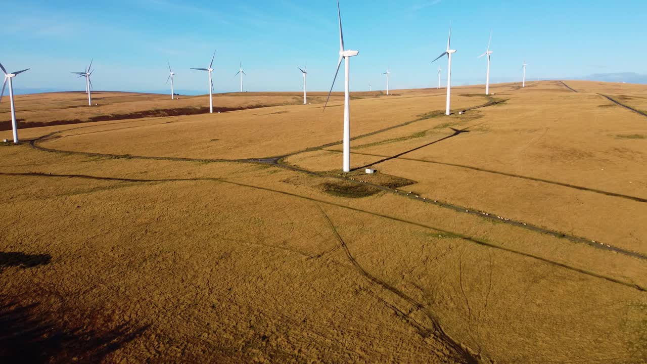 Tilt Up Drone Reveal of Large Wind Farm Over Natural Mountain Landscape with Bright Blue Sky. Renewable Sustainable Energy Generation