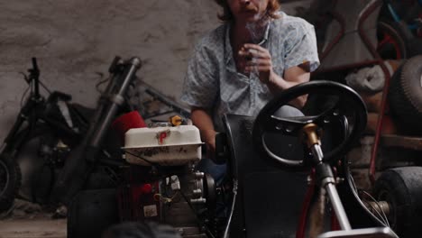 cinematic shot of mechanic inspecting a go-kart seat while smoking a cigarette