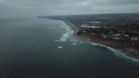 View-from-a-drone-flying-really-over-the-sea-showing-a-beach,-the-coast-and-the-town-near-the-ocean